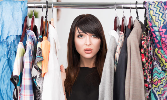 Portrait of young confused woman in front of a wardrobe full of clothes. Nothing to wear concept